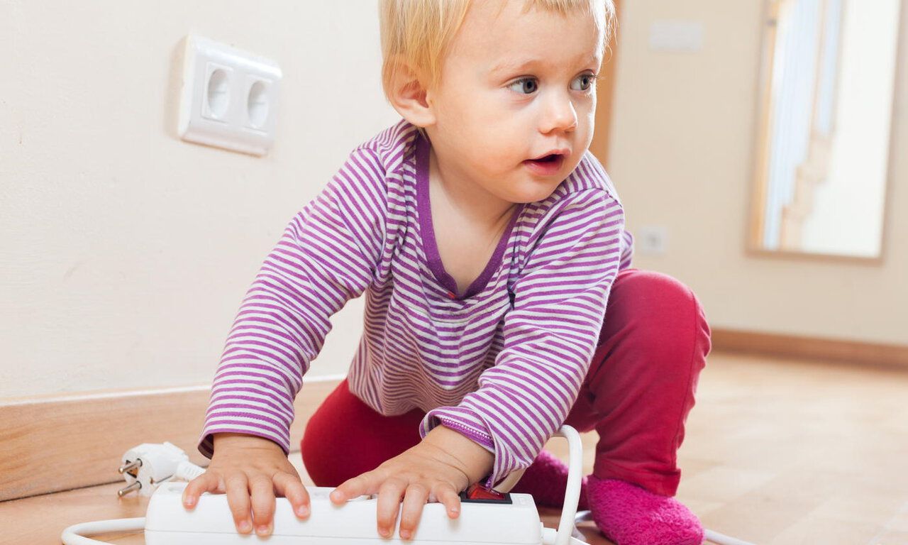 Baby girl playing with electrical extension  on floor at home