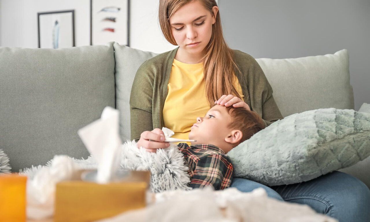 Woman measuring temperature of her sick son at home