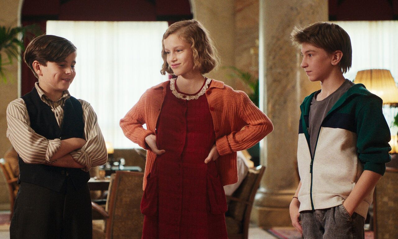 Szene aus dem film Das geheime Stockwerk, drei Kinder stehen in einem nostalisch eingerichteten Salon