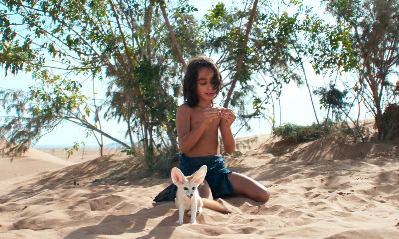 Ein Kind und ein Wüstenfuchs sitzen zusammen im Wüstensand