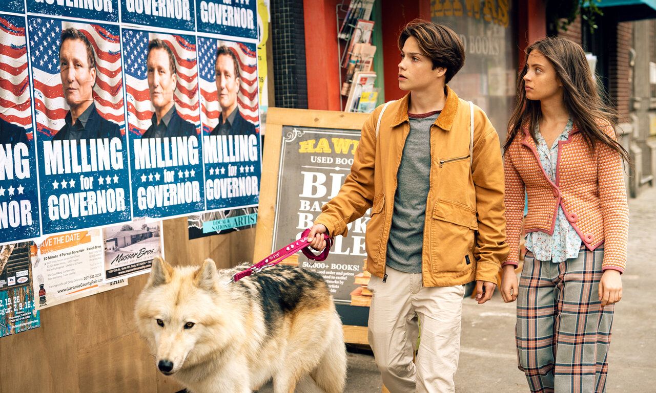 Szene aus dem Film Woodwalkers 2, ein Junge undein Mädchen laufen mit einem Hund an Wahlplakaten vorbei