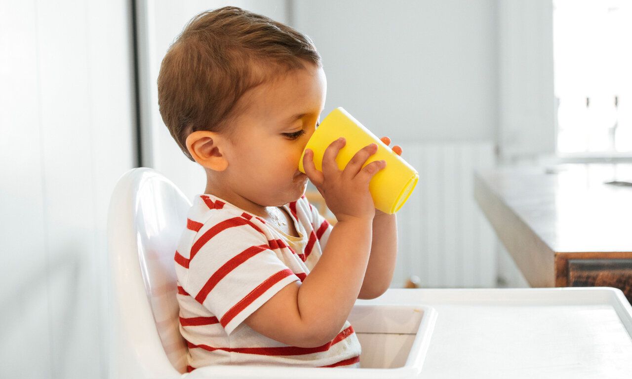 Junge sitzt in einem Hochstuhl und trinkt aus gelbem Becher