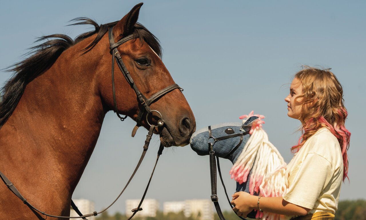 Szene aus dem Film Pferd am Stiel, ein Mädchen mit einem Steckenpferd steht einem echten Pferd gegenüber