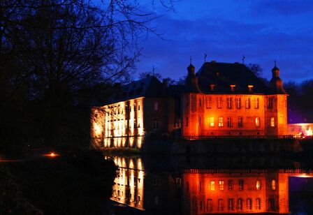 Schloss Dyck bei Nacht, rot angestrahlt, Spiegelung im Wassergraben