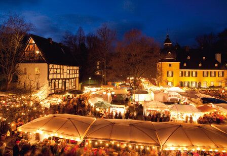 Weihnachtsmarkt Schloss Lüntenbeck am Abend, Verkaufsstände vor Fachwerkhaus und Schloss festlich beleuchtet