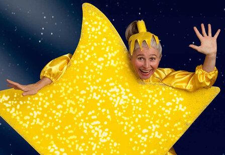 Frau als gelber Stern verkleidet, lacht in die Kamera, dunkler Hintergrund