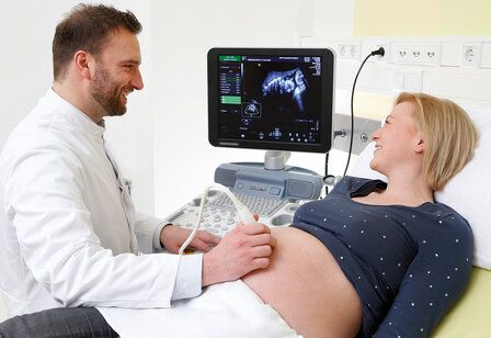 Ein Arzt macht eine Ultraschalluntersuchung bei einer Schwangeren, beide lächeln