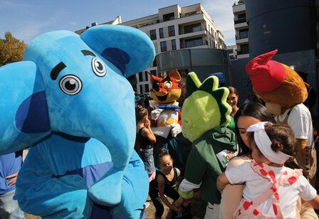 Der blaue Elefant vom Kinderschutzbund und andere verkleidete Figuren in einer Gruppe von Eltern und Kindern, auf der Wiese vorm Landtag