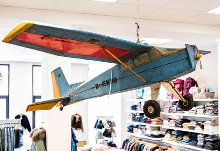 Ein großes Holzflugzeug hängt im Innenraum eines Ladenlokals, im Hintergrund Kindermode