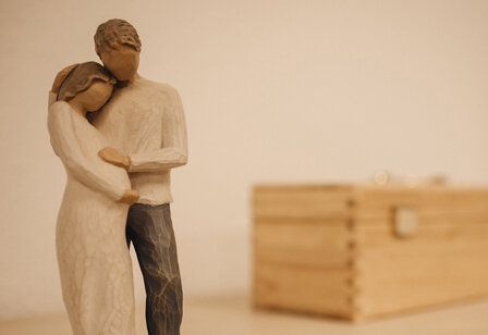 Holzfiguren, eine schwangere Frau und ein Mann, der sie umarmt und den Bauch streichelt
