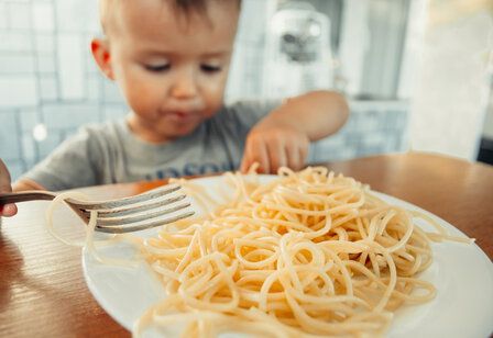 Kleinkind in der Küche Nudeln essend mit Gabel und Fingern