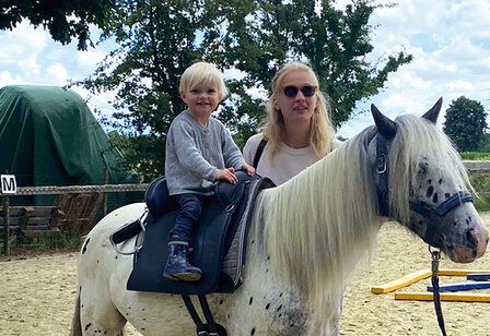 Kind sitzt auf einem Pony, Mutter steht daneben