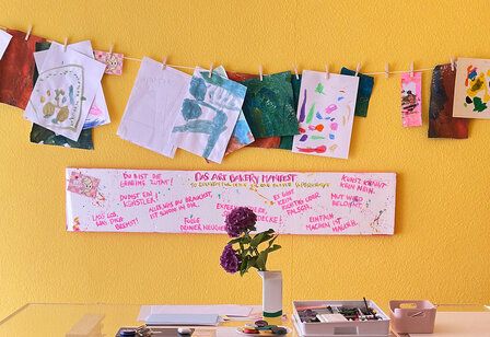 Art Bakery, Tisch mit Malutensilien und Hortensie vor gelber Wand, gespannte Leine mit Kinderbildern