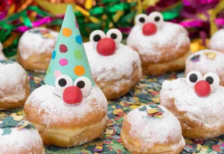 Karnevalsgebäck Berliner mit Augen und Nasen und Hütchen, auf Tisch mit Konfetti und Luftschlangen