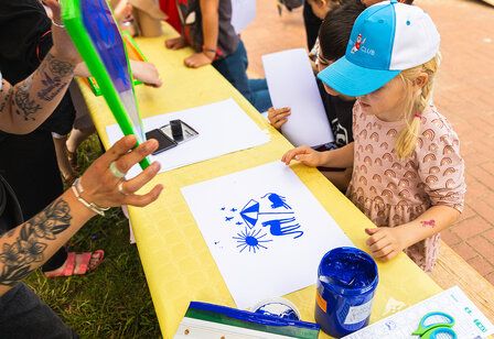 kleines Mädchen steht an einem Aktionstisch bei der Konferenz der Kinder, auf dem Tisch liegt ein gemaltes Bild