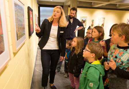 Eine Museumsführerin steht mit Kindern vor einem gemälde und erklärt es.