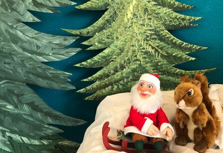 Weihnachtspüppchen und Plüscheichhörnchen sitzen zusammen vor Tannenkulisse