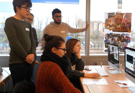 zwei Jugendliche sitzen an einem Schreibtisch und arbeiten an Computern, drei Jugendliche stehen dahinter und gucken zu, Düsseldorfer Jugendmedientage