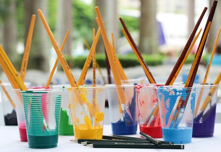 verschiedene Plastikbecher mit bunter Farbe und Pinseln