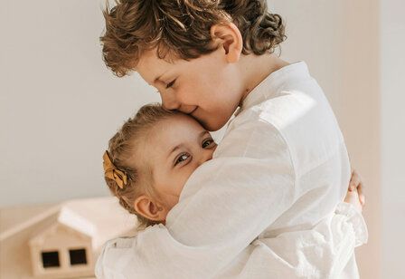 Geschwisterpaar umarmt sich, die kleine Schwester lacht in die Kamera, der große Bruder hat die Augen geschlossen 