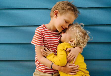 Zwei Jungs umarmen sich, im Hintergrund: blaue Wand