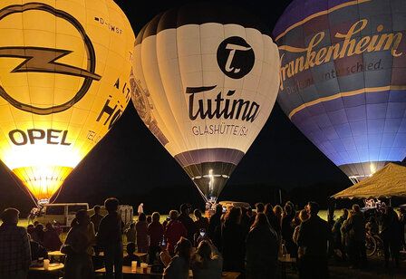 drei Heißluftballons in der Nacht, am Boden. Publikum davor
