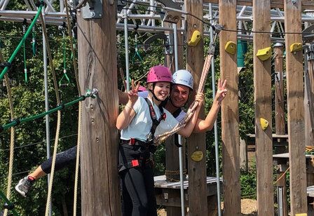 ein Mädchen und eine Frau beim Klettern im Hochseilgarten, zeigen lachend Victory-Zeichen
