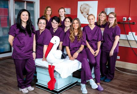 Das Team der Entbindungsstation steht in violetten Anzügen im Kreißsaal