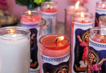Kerzen in Glasbehältern mit Heiligenmotiven stehen nebeneinander