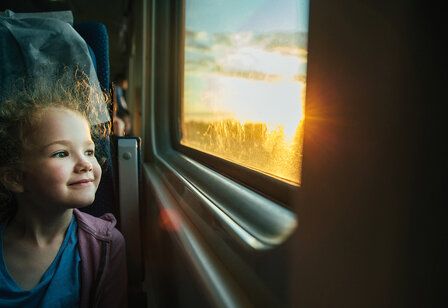 Mädchen sitzt im Zug und schaut aus dem Fenster