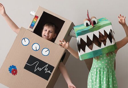 Kinder mit Kostümen aus Pappkartons: Junge als Roboter, Mädchen als Krokodil verkleidet