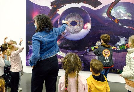 Museumsführerin steht mit Kindern vor einem Kunstwerk und erklärt es