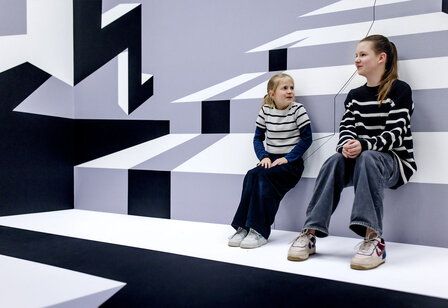 zwei Mädchen sitzen in einem grafisch gestalteten Raum im Kunstpalast