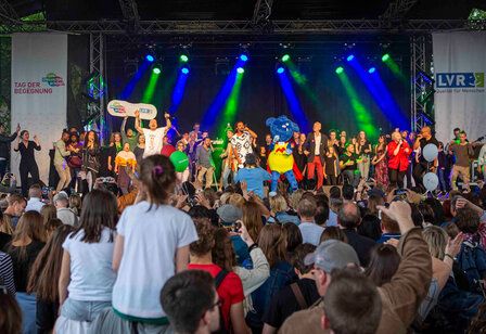 Open-Air-Bühne, auf der sehr viele Menschen singen und tanzen, avor Publikum