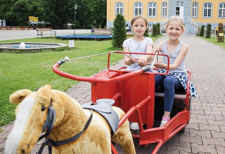 Zwei Mädchen in einer Kutsche mit Plüschpferd, im Hintergrund Schloss Beck