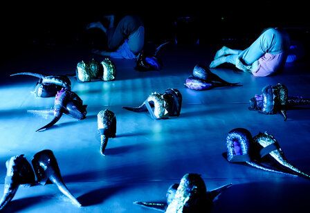 My tail and I Tanzperformance, blaue Beleuchtung, zwei Kinder liegen mit den beinem über dem Kopf auf der Bühne, glitzernde Dino-Schwänze liegen herum