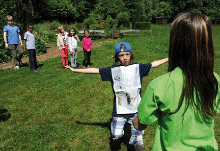Ein Junge läuft über eine Wiese zu einer Frau, andere Kinder gucken zu