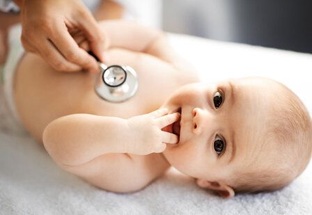 Ein Baby liegt auf dem Rücken und wird mit einem Stethoskop abgehört