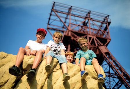 Vier Jungs sitzen auf einem Felsen, im Hintergrund ein Förderturm