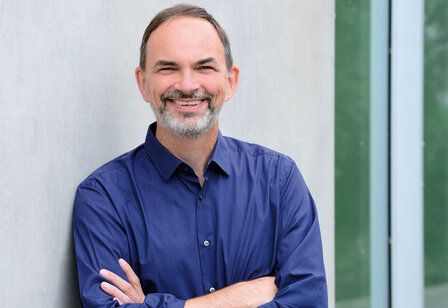 Prof. Dr. Ulrich Reinhardt steht mit verschränkten Armen vor grauer Mauer