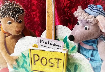 Ein Stoffigel und eine Stoffmaus sitzen zusammen, zwischen ihnen ein Briefkasten mit einer Einladung