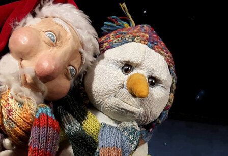 Puppen in Form von Weihnachtsmann und Schneemann gucken den Betrachter an, der Hintergrund ist schwarze Nacht