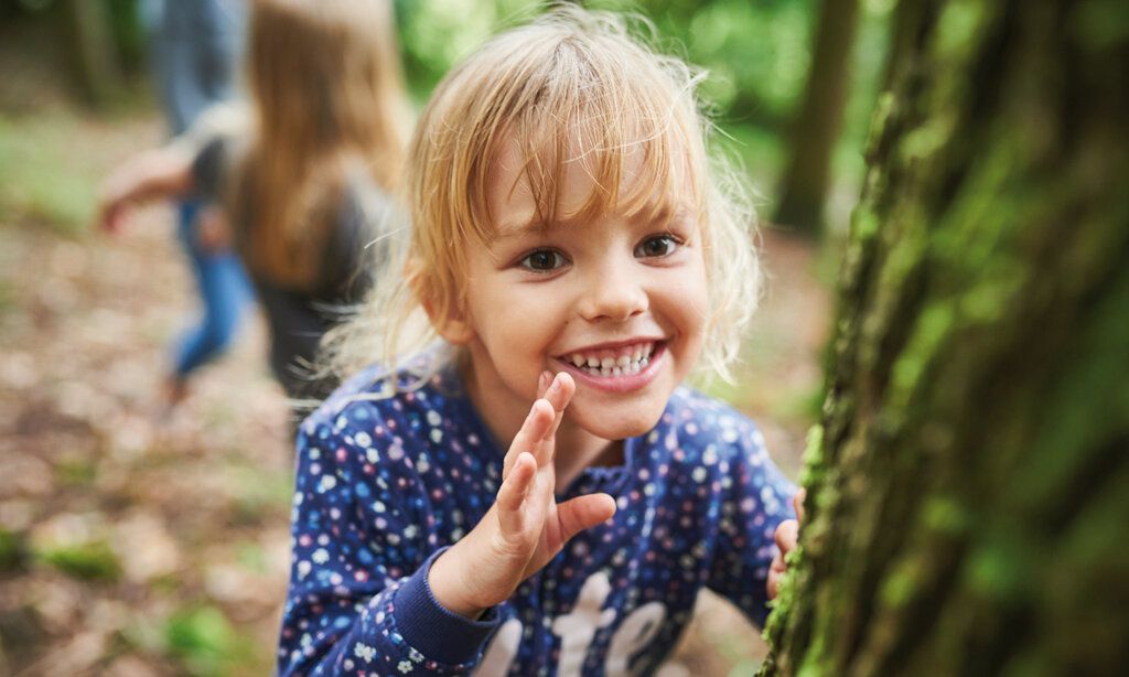 kleines Mädchen steht lachend an einem Baum im Wald