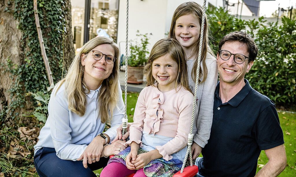 Vater, Mutter und zwei Töchter im Garten, ein Mädchen sitzt auf der Schaukel