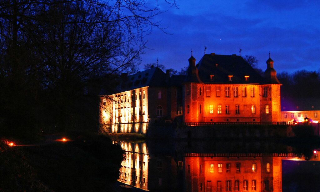 Schloss Dyck bei Nacht, rot angestrahlt, Spiegelung im Wassergraben