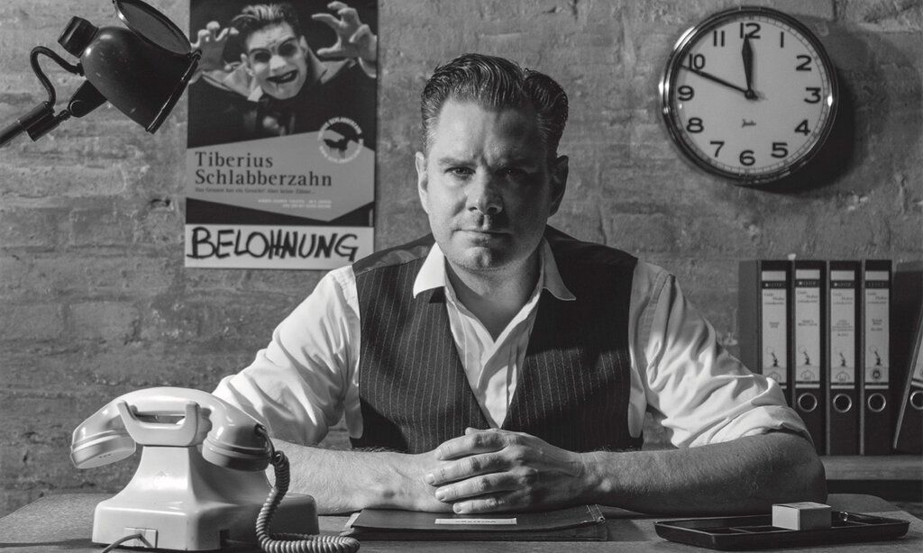 Guido Hoehne sitzt in einem Büro am Schreibtisch, Schwarz/Weiß-Foto