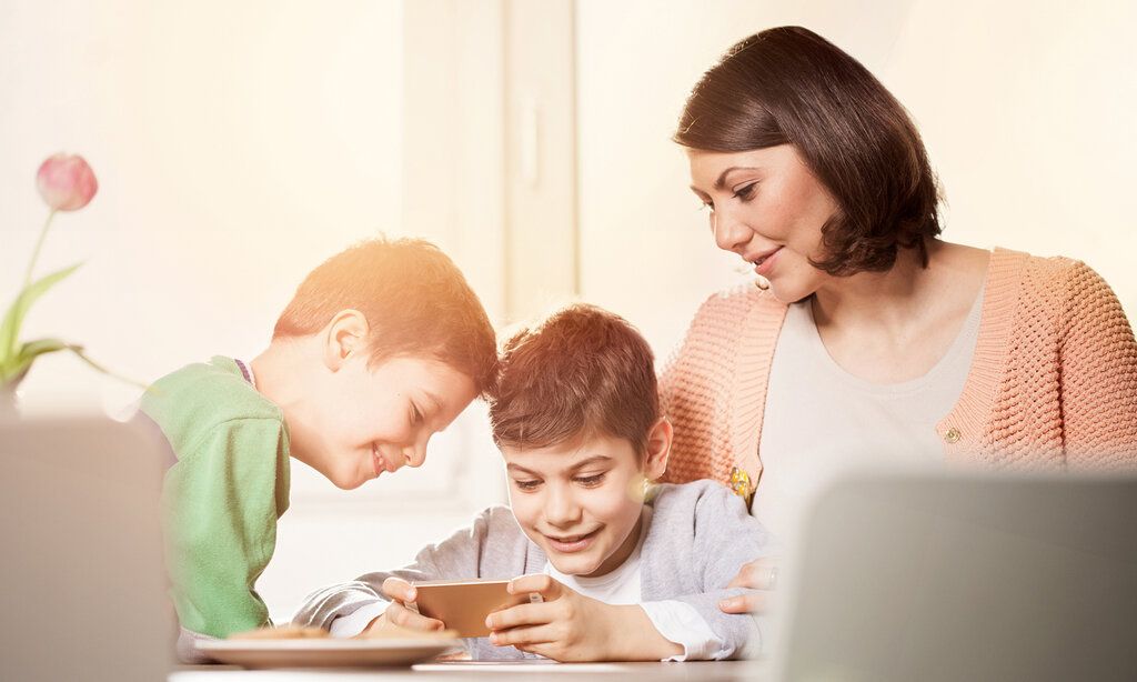 Zwei Söhne spielen mit dem Smartphone, Mutter schaut zu