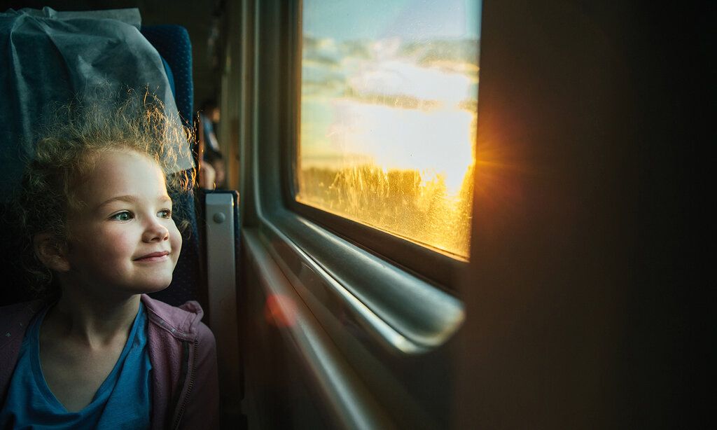 Mädchen sitzt im Zug und schaut aus dem Fenster