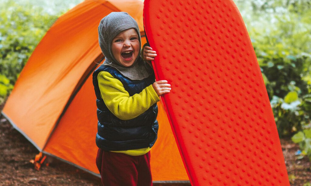 Ein Kind steht vor einem Zelt mit einer Luftmatratze und lacht