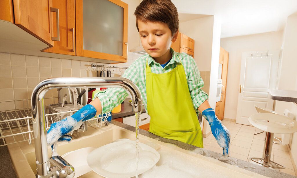 Ein Junge steht mit blauen Gummihandschuhen am Spülbecken und macht den Abwasch